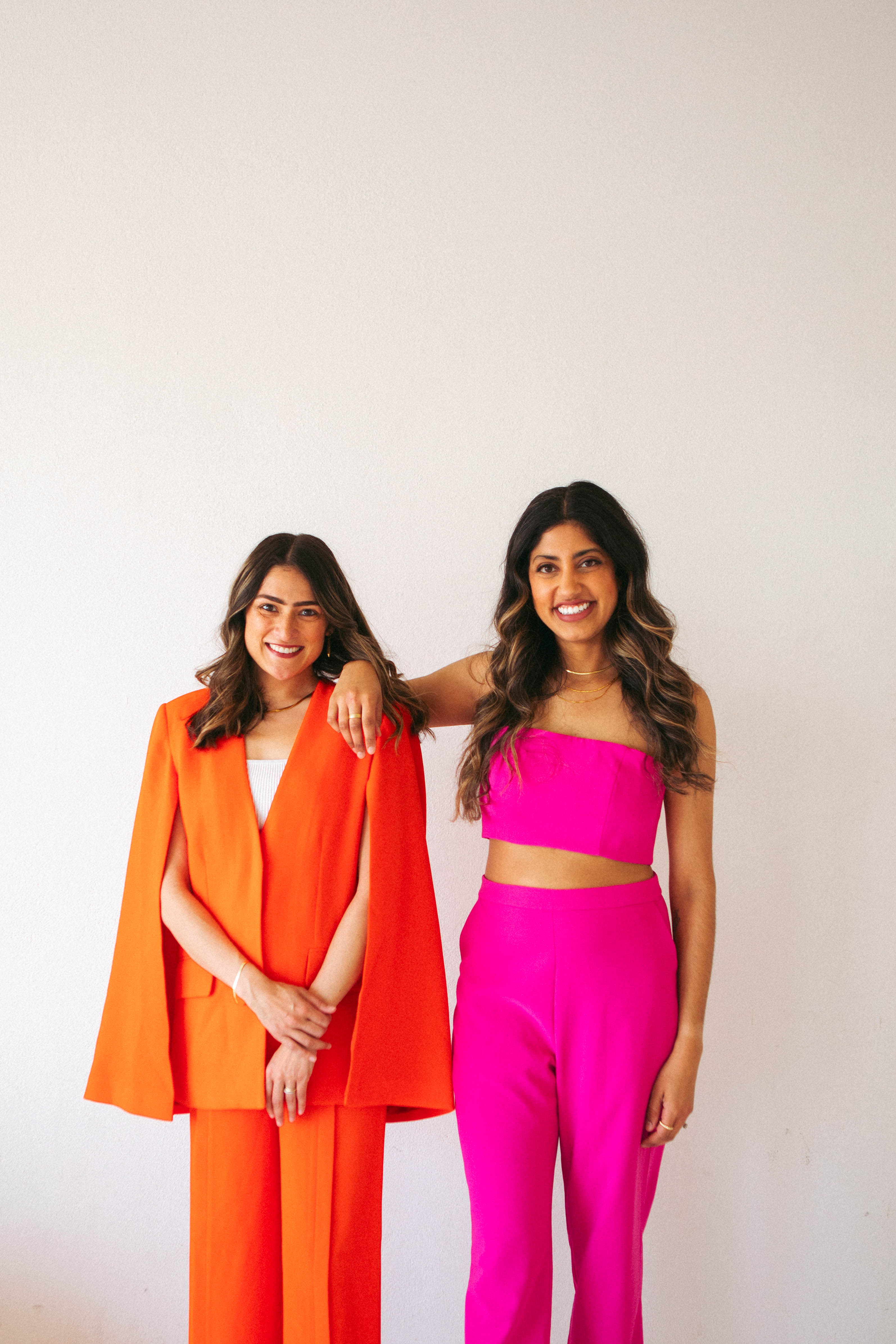 Purvi and Karen standing together in bright orange and pink outfits, smiling
