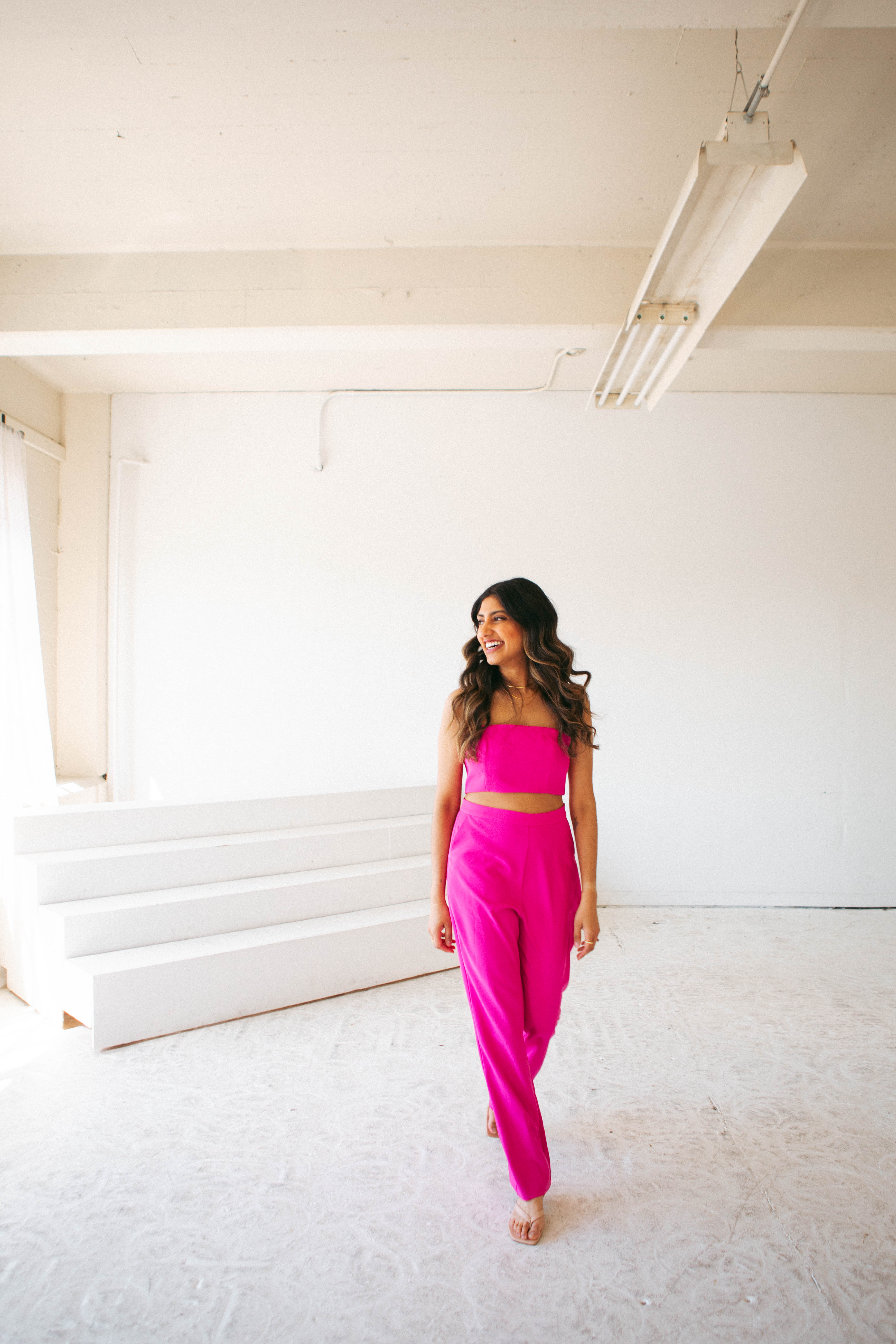 Purvi Vyas in a bright pink outfit, laughing in a white studio